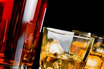 whiskey with ice in glasses near bottle on black background
