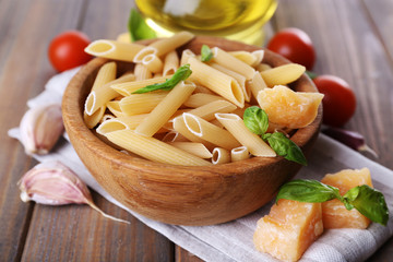 Raw pasta in bowl with cheese and vegetables on table close up