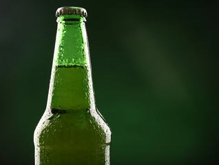 Glass bottle of beer on dark green background
