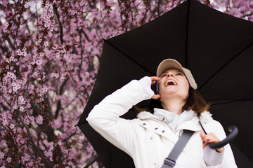 Woman with hat and umbrella talking on the phone in spring