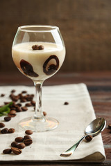 Glass of tasty panna cotta dessert on plate, on wooden table