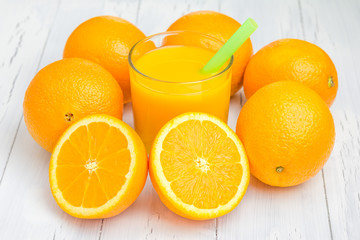 Glass of orange juice and oranges on white table