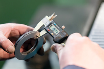 Factory worker measuring detail with digital Vernier Caliper