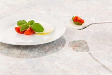 Mozzarellasalat mit Tomaten und Basilikum auf einer Gabel
