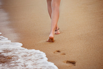 Healthy young woman is walking on the yellow sand leaving footpr