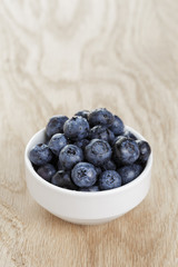 heap of fresh washed blueberries in white bowl on wood table