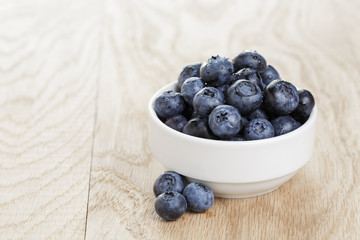 heap of fresh washed blueberries in white bowl on wood table