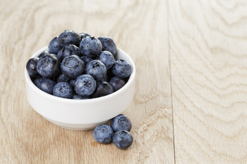 heap of fresh washed blueberries in white bowl on wood table