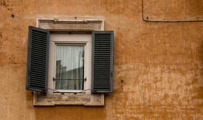 Fototapeta na wymiar A Roman window, with shutters, set in an ochre coloured wall