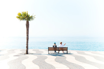 Couple on vacation sitting on a bench observing the sea