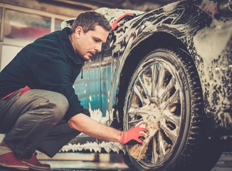 Man worker washing car's alloy wheels on a car wash