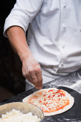 Chefs are sprinkle cheese onto a pizza