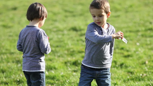 Two boys in the park, blowing and chasing soap bubbles