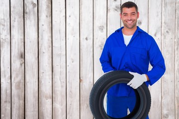 Composite image of mechanic holding tire on white background - Powered by Adobe