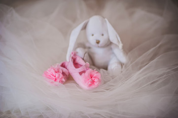 Fototapeta na wymiar Pink booties with flowers near the white rabbit toy, decor, life