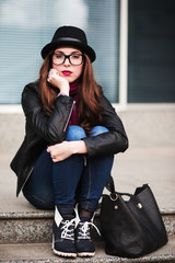 Fototapeta premium the stylish city girl in sunglasses sits on steps