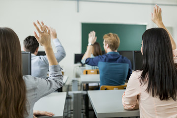 Naklejka na ściany i meble Young students raising hands in a classroom
