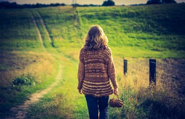Girl in sweater walking by rural grassy road - 81368589