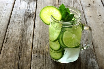 Detox water with lime and cucumbers in a mason jar against wood