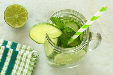 Detox water with lime and cucumbers in a jar on white marble