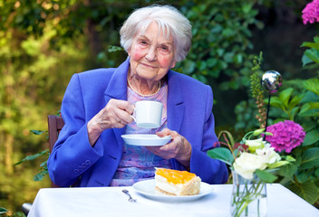 Elderly Woman Drinking Coffee at the Garden Table.
