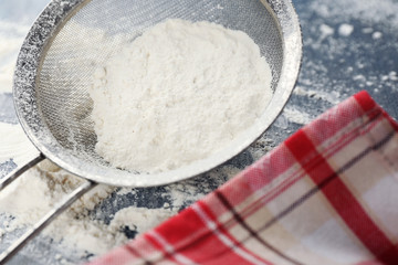 Sifting flour through sieve on wooden table, closeup