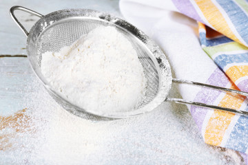 Sifting flour through sieve on wooden table, closeup
