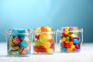 Colorful candies in jars on table on blue background background