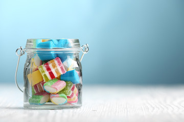 Colorful candies in jar on table on blue background