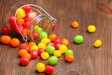 Colorful candies in jar on wooden background