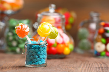 Colorful candies in jars on table on wooden background