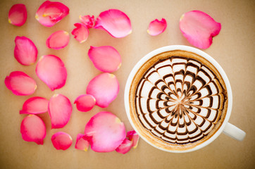 A cup of coffee with latte art and petals rose on brown paper ba