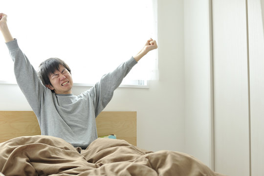 ベッドの上で眠そうにしているパジャマ姿の男性