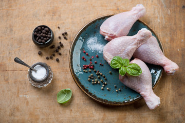 Raw chicken legs with various spices on a rustic wooden surface