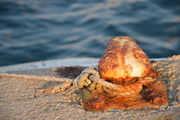 rostiger Poller mit Seil in der Abendsonne