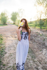 Red-haired young lady with bouquet of daffodils at countryside