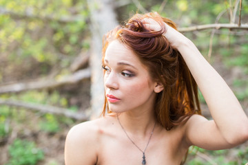 Spring portrait of a red-haired young lady touching her hair