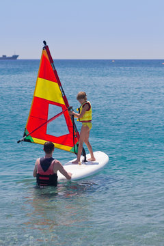Little girl taking a lesson of windsurfing on a calm sea. Instructor and student or father and daugher. Learning new skills at young age