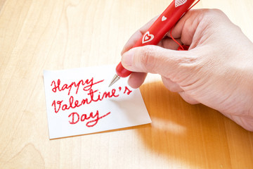Hand holding red pen with white heart pattern, writing on blank