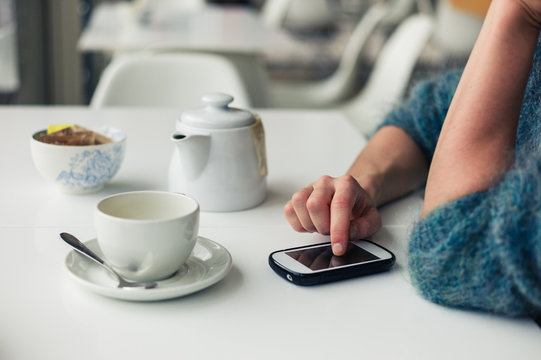 Woman using phone and having tea