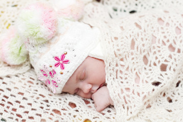Baby in hat lies on bed under soft white knitted shawl and sleep