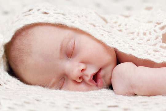 Peaceful baby lying on bed with soft white knitted blanket