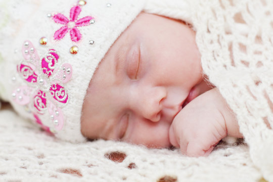 Baby lying in hat on bed under soft white knitted shawl