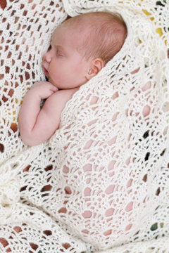 Peaceful baby lying on bed under soft white knitted shawl