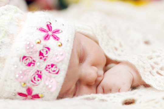 Cute baby lying in hat on bed under soft white knitted shawl