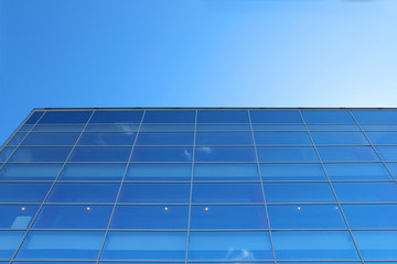 Glass wall of building with reflection of blue sky with small 