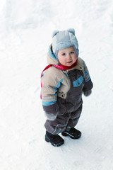 Little boy wearing warm jumpsuit stands on snow and smiles 