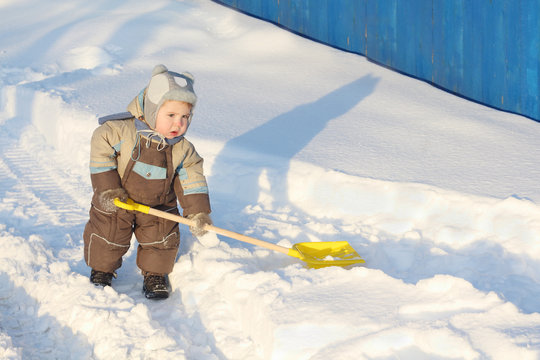 Little handsome boy wearing jumpsuit holds shovel on snow 