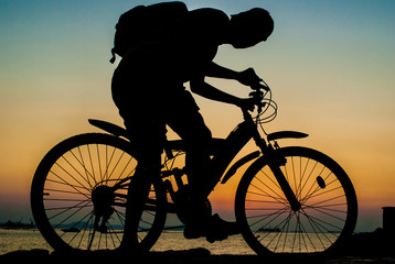 Fototapeta premium Silhouette of backpacker ride mountain bike on bridge beside sea