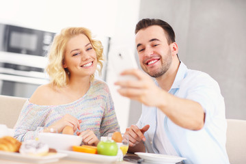 Obraz na płótnie Canvas Happy couple eating breakfast and taking selfie